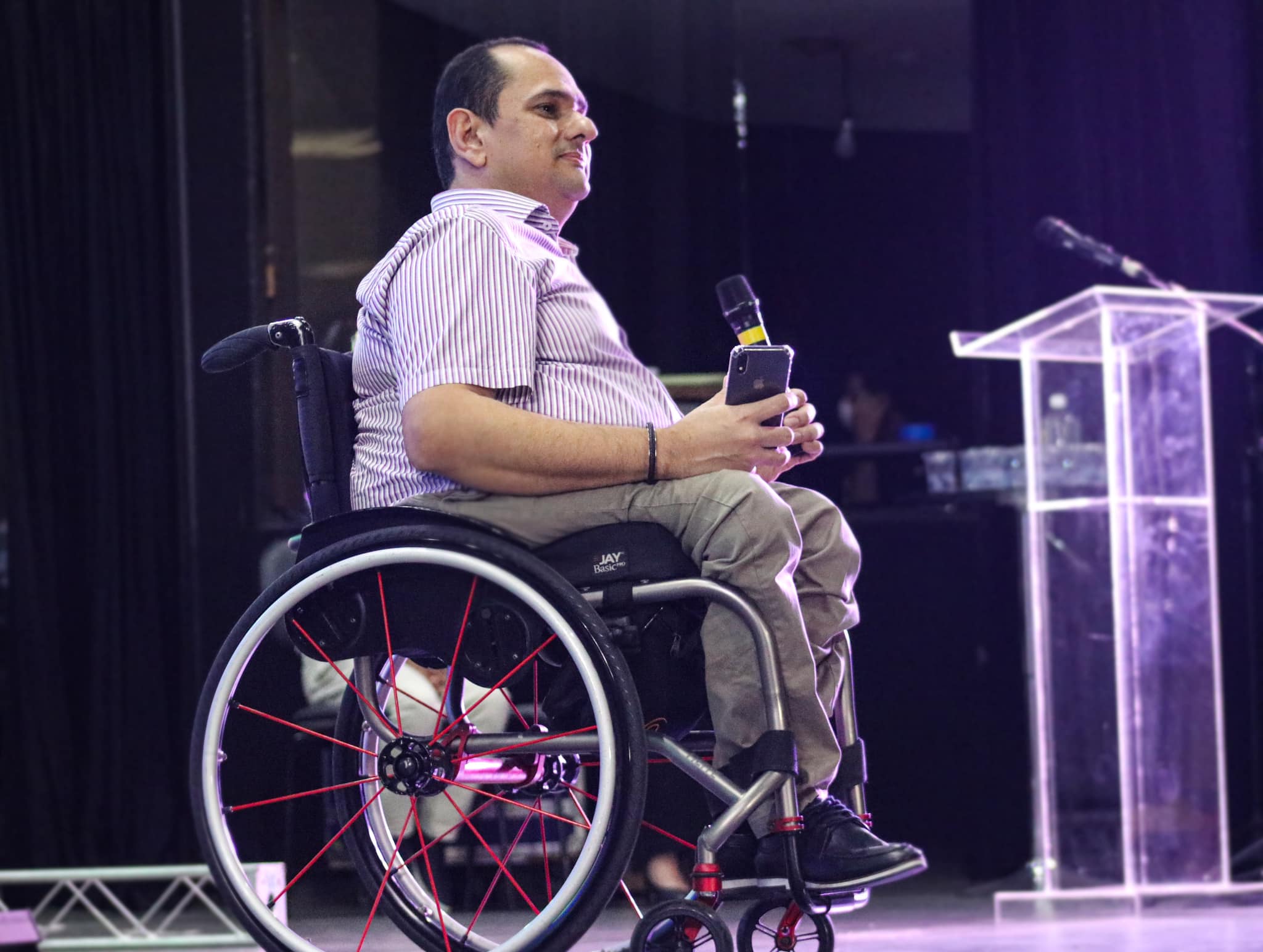 O jornalista Jairo Marques no palco. Ele fala ao microfone e usa uma cadeira de rodas.