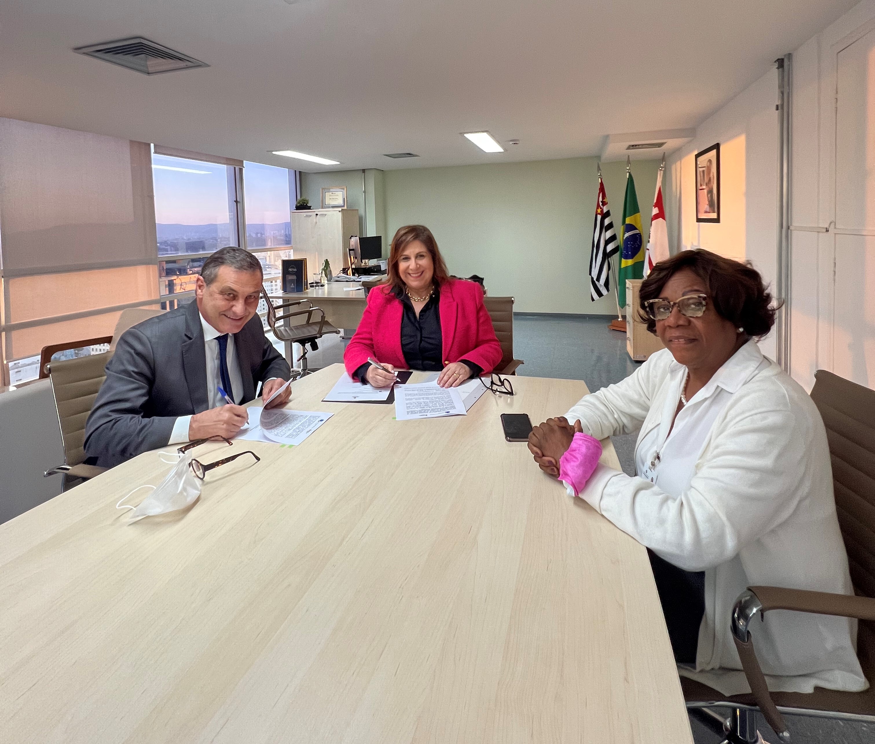 sentados ao redor de uma mesa, no gabinete da SMPED, o presidente do TRE-SP, Desembargador Paulo Sérgio Brant de Carvalho Galizia, a secretária municipal da SMPED Silvia Grecco e asecretaria municipal da Justiça, Eunice Prudente. Eles estão sorrindo para a foto. A secretaria Silvia e o Desembargador Paulo Sérgio Brant de Carvalho Galizia assinam o termo.