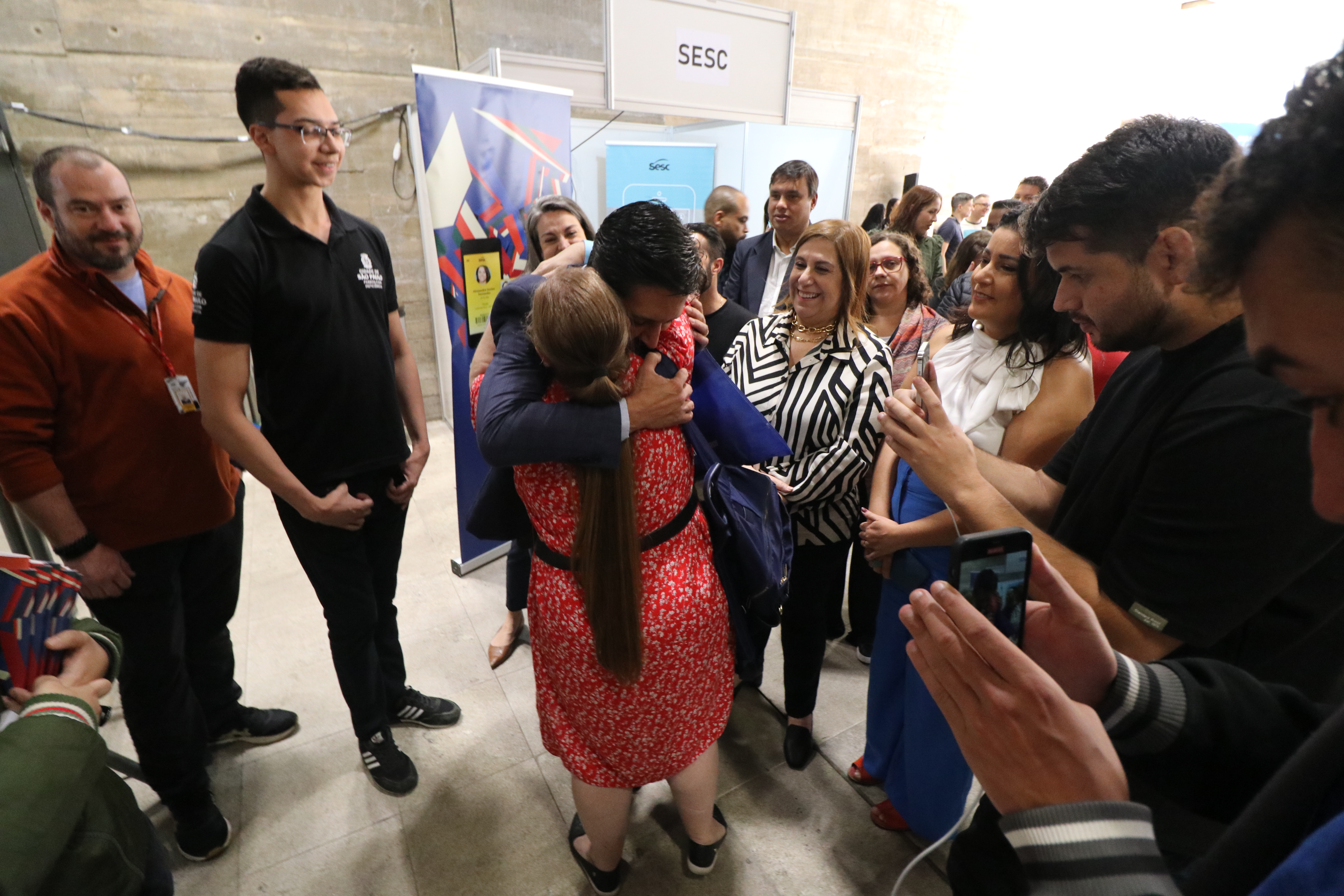 Prefeito Ricardo Nunes abraçando uma mulher. Em volta há autoridades e pessoas que estão participando do mutirão.