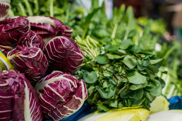 Foto de algumas verduras, repolhos roxos e maços de rúcula.