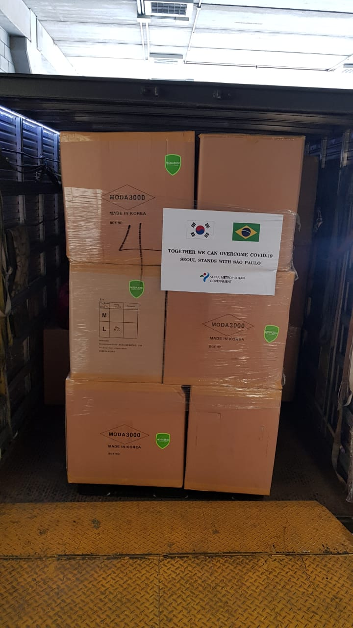 Foto das caixas da doação em um container, com as bandeiras da Coreia do Sul e do Brasil impressas em uma folha que está colada a caixa. 