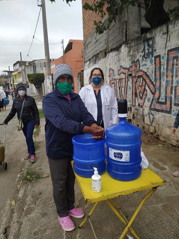 #PraCegoVer: Fotografia dos agentes de saúde auxiliando os moradores na zona norte sobre como lavar as mãos