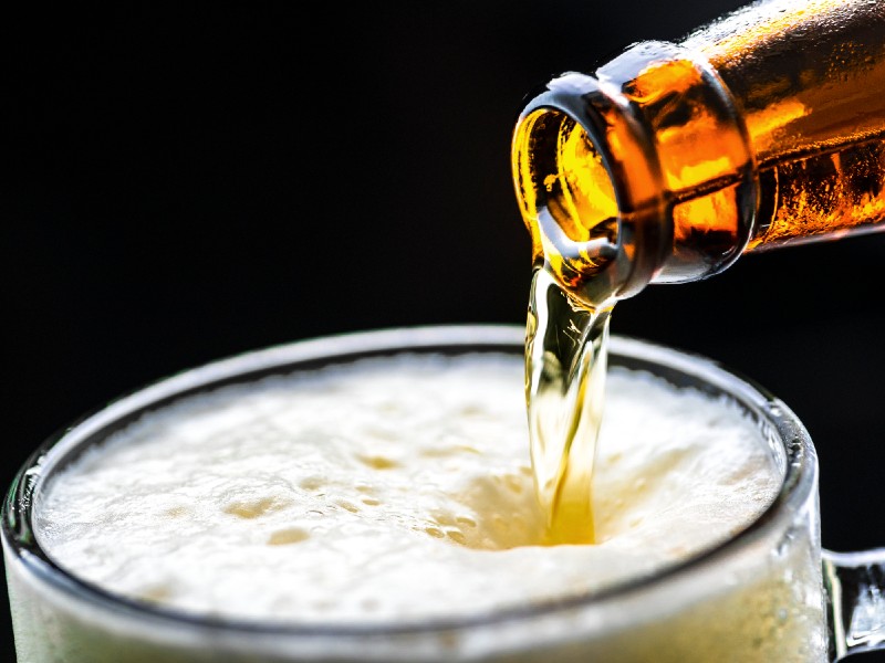 A foto mostra uma garrafa de cerveja e a bebida sendo derramada em um copo
