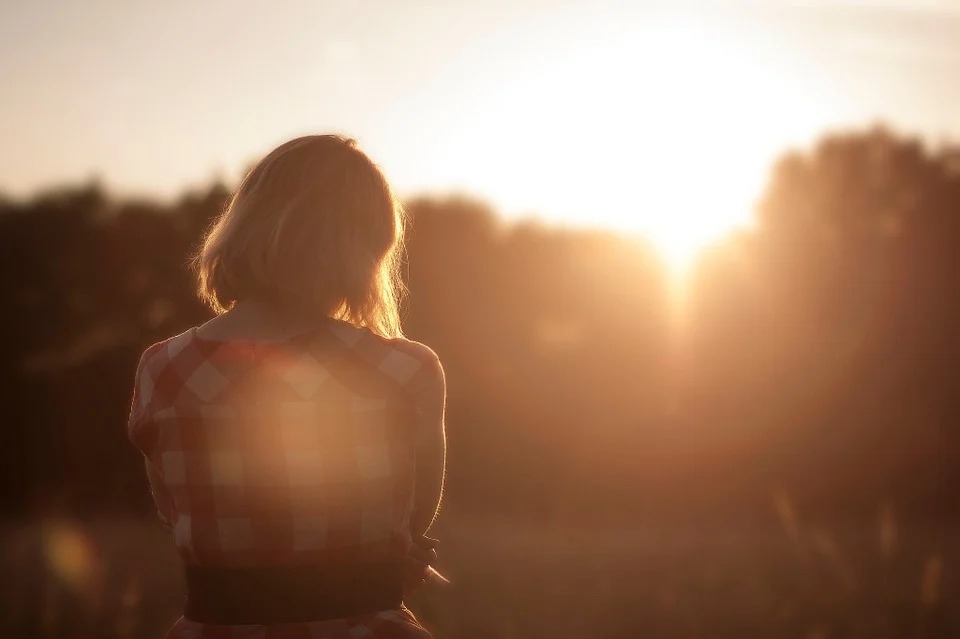 De costas uma mulher observa o horizonte, ela está sozinha na natureza  diante do por do sol