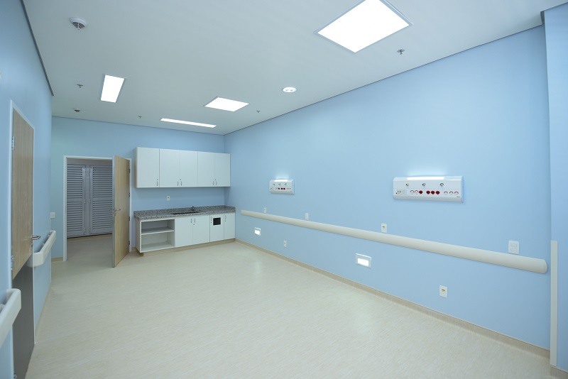 #PraCegoVer: a foto mostra uma sala/leito com paredes azuis, uma pia com gabinete e um armário aéreo