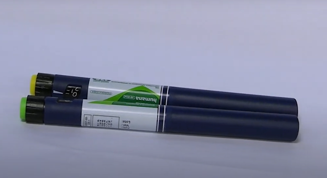 Em cima de um fundo totalmente branco estão duas canetas de insulina. Elas possuem a embalagem azul, com um rótulo branco com detalhes em verde. A ponta de uma é verde e a da outra, amarela.