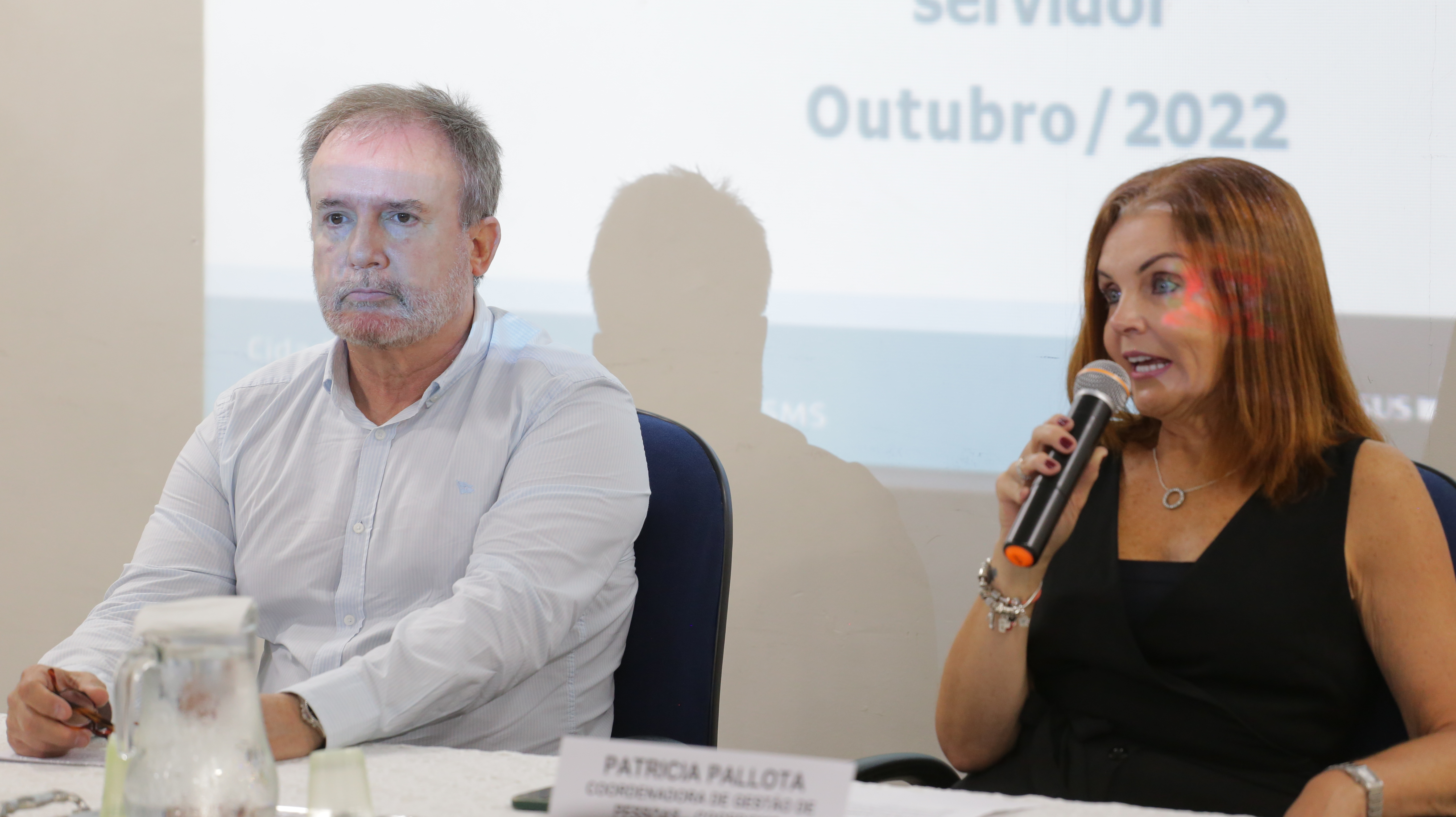 Na imagem estão sentados o secretário da Secretaria Municipal da Saúde, Doutor Luiz Carlos Zamarco, e, do  seu lado direito, a coordenadora de gestão de pessoas, Patrícia Pallota, que está falando ao microfone