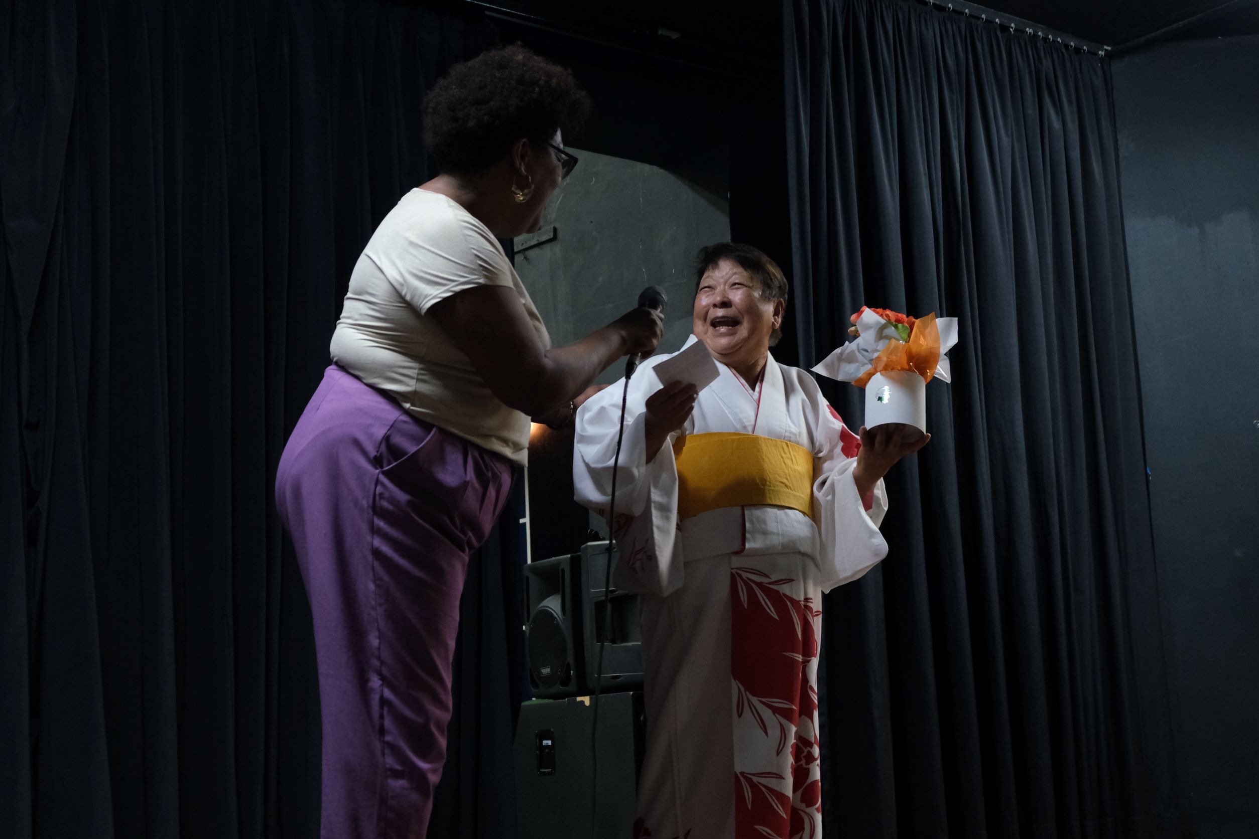 Na imagem está a apresentadora do evento, Ana Cecília da Divisão de Carreiras e Qualidade de Vida no Trabalho, conversando com uma integrante do grupo de dança folclórica japonesa.