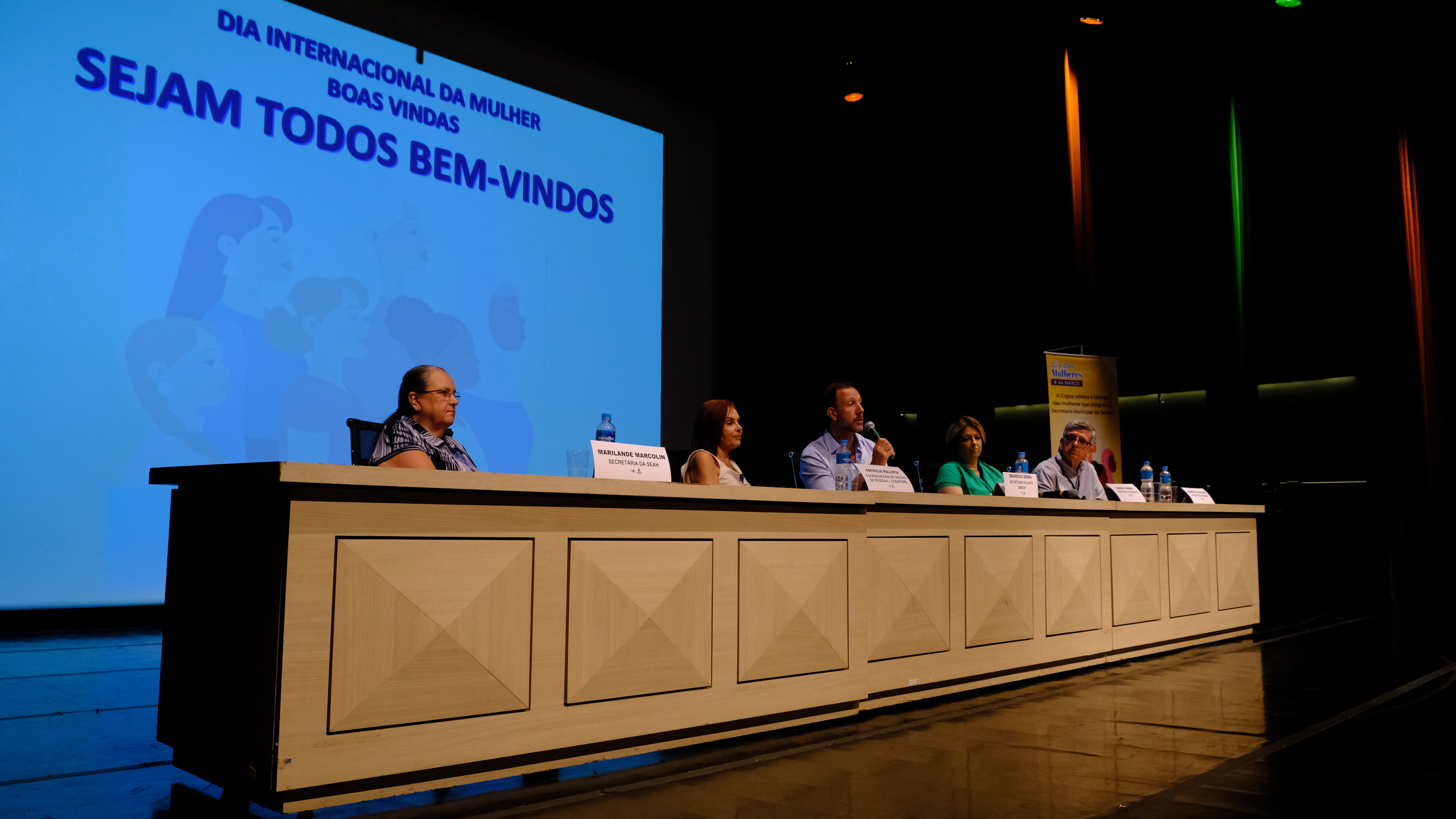 Maurício Serpa, Sandra Sabino, Marilande Marcolin, Patrícia Pallota e o Benedicto Accacio compõem uma mesa que está localizada no centro da imagem.  Maurício Serpa fala ao microfone.