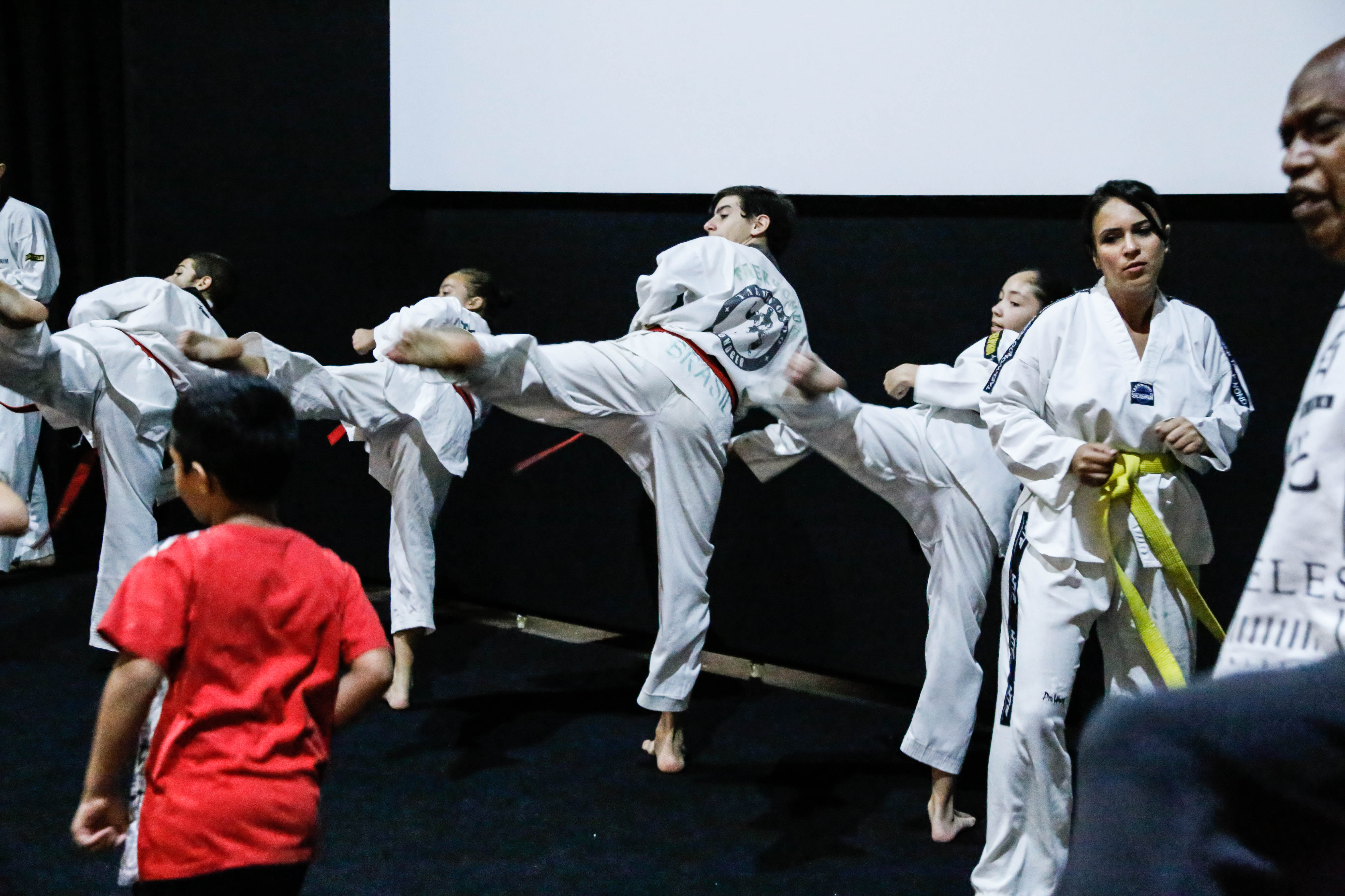 Apresentação de tae-kwon-do. Alunos chutam o ar em sincronia.