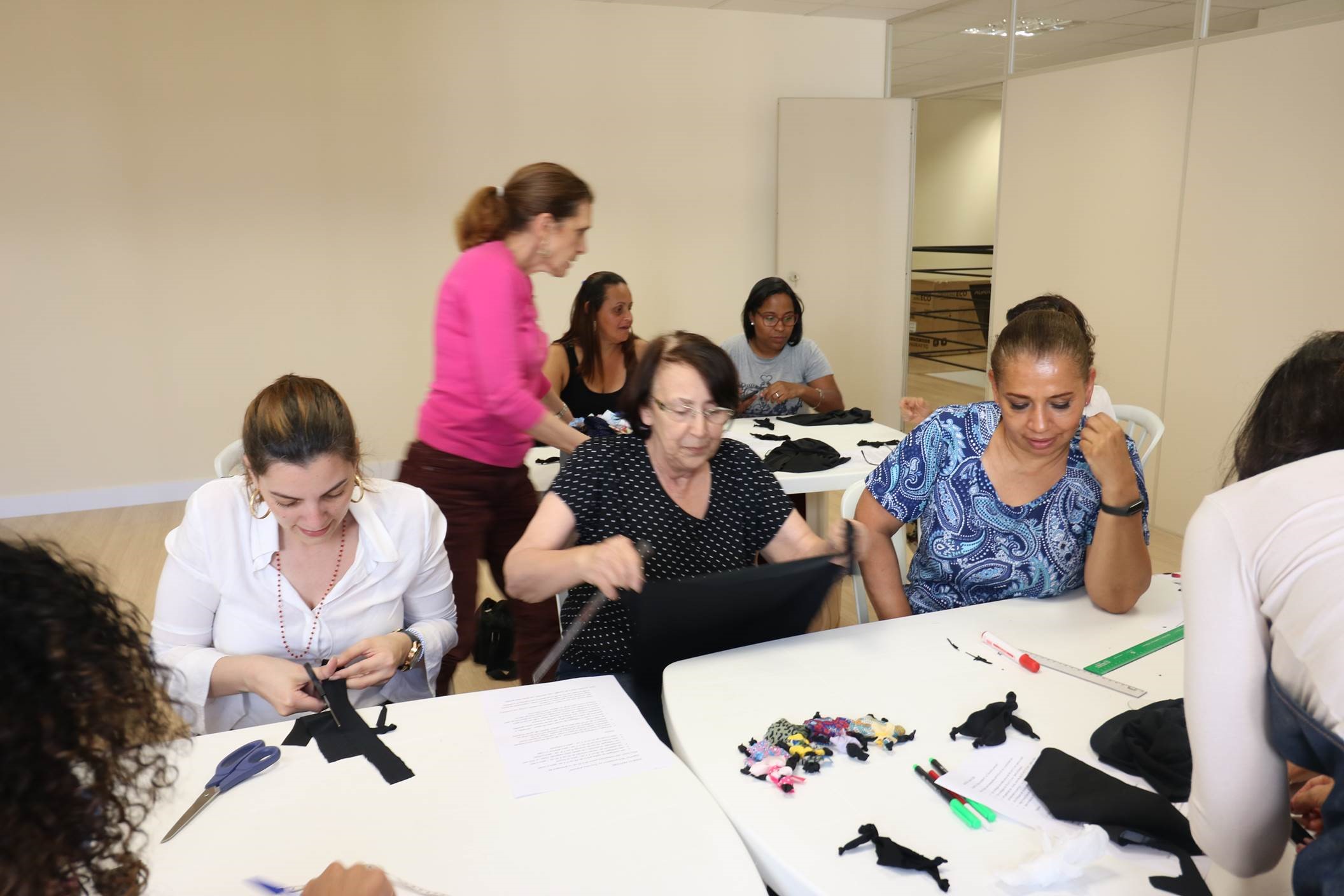 #Paracegover Na imagem está sendo realizada a oficina de bonecas Abayomi. As mulheres estão recortando os tecidos para criarem as bonecas.