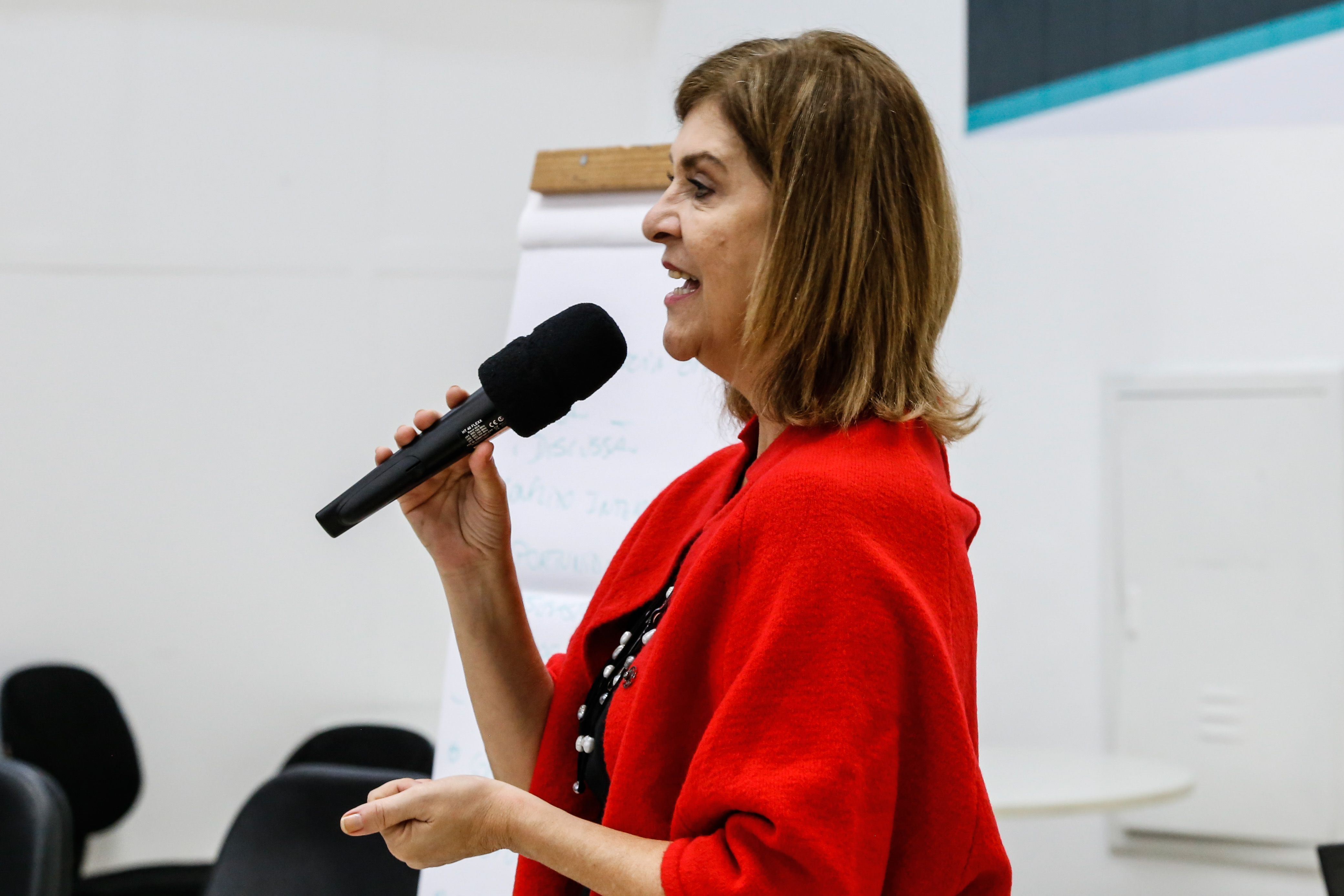 #Paracegover Na imagem: a coordenadora de Gestão de Pessoas da Secretaria Municipal de Saúde, Jane Abraão Marinho, está com um microfone na mão dando as boas vindas na abertura do evento