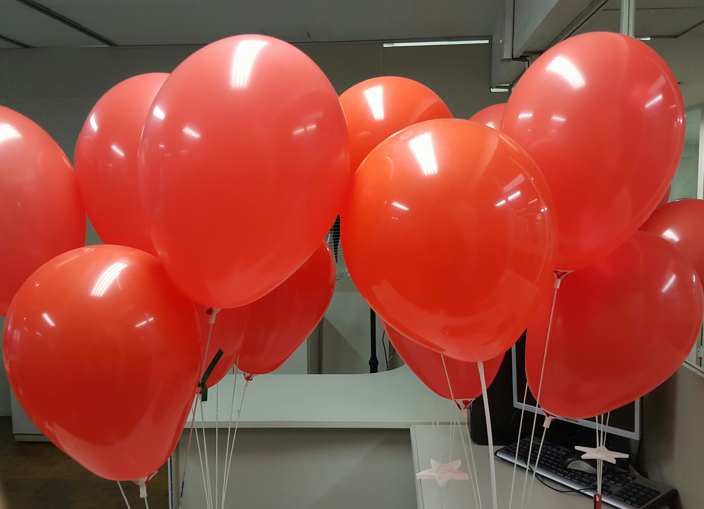 #Paracegover Na Imagem estão diversos balões vermelhos estão presos a um suporte em cima de uma mesa.