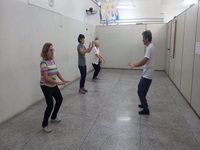 Ao lado direito está o instrutor de DAO-in ensinando a prática. Ao lado esquerdo da imagem estão três mulheres seguindo as instruções e realizando a prática da Dao-in.