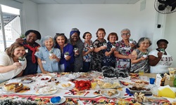 Na imagem estão váris mulheres atrás de uma mesa com um banquete. Todas sorriem. 