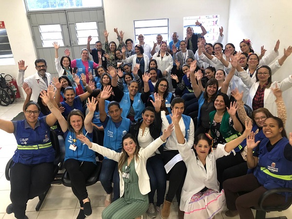 #PraCegoVer: na imagem há muitos profissionais de saúde numa sala. Todos estão com os braços levantados, como se estivessem comemorando.