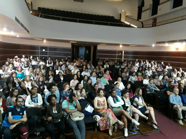 Há dezenas de pessoas sentadas nos assentos do anfiteatro do Colégio Caetano de Campos durante o Encontro de Práticas Intergrativas e Complementares em Saúde