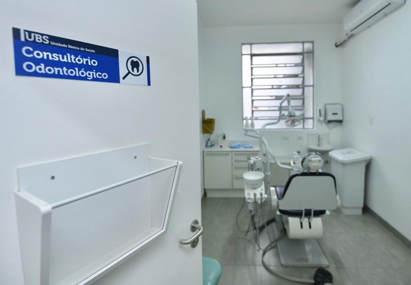 Foto de consultório odontológico. À esquerda da imagem, uma porta com uma placa azul com letras brancas diz 