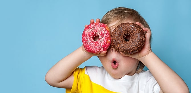 Imagem de um menino loiro em um fundo azul, segurando duas rosquinhas doces