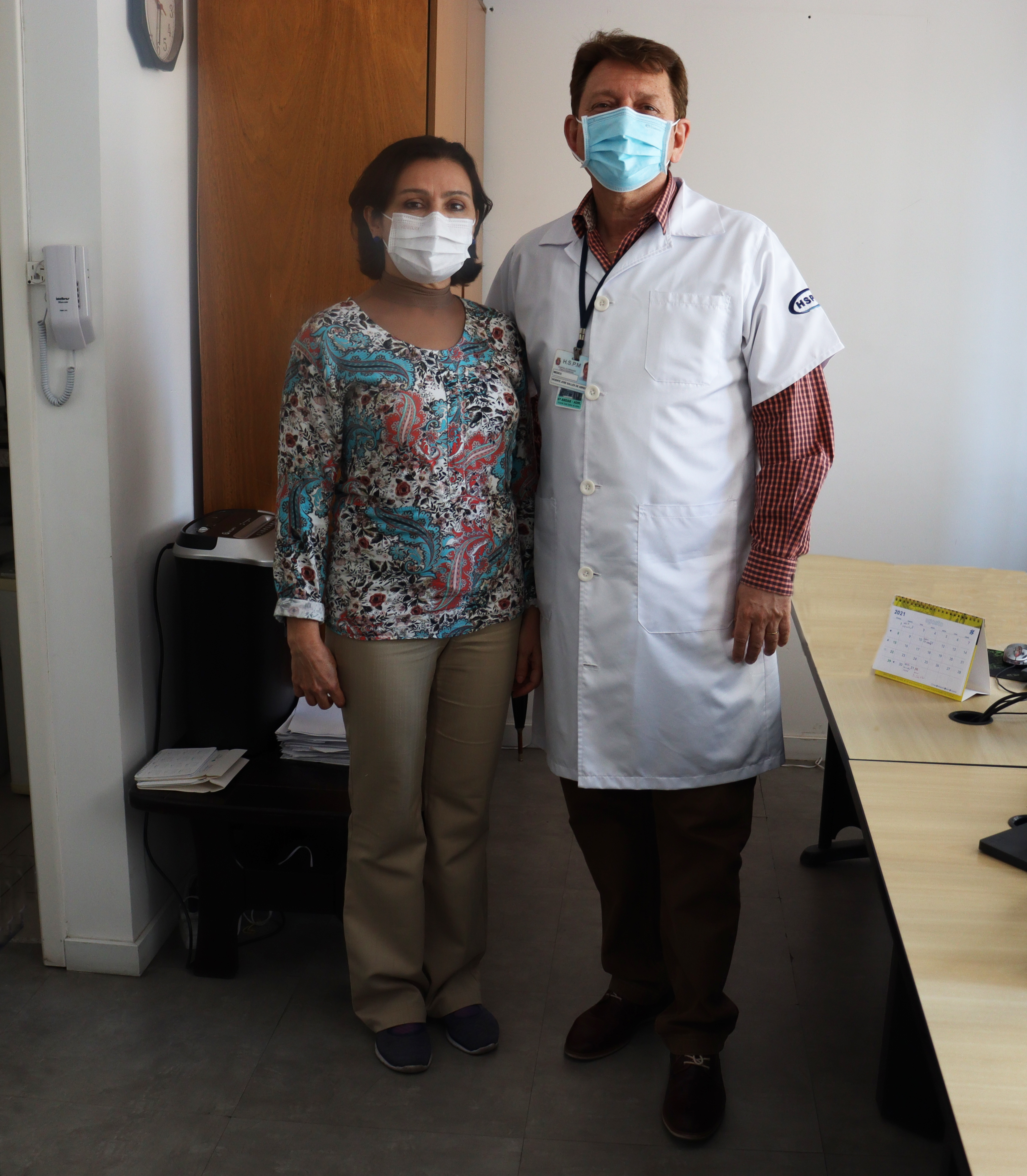 Foto de dois médicos do hospital, uma mulher a esquerda e um homem a direita, em uma sala administrativa