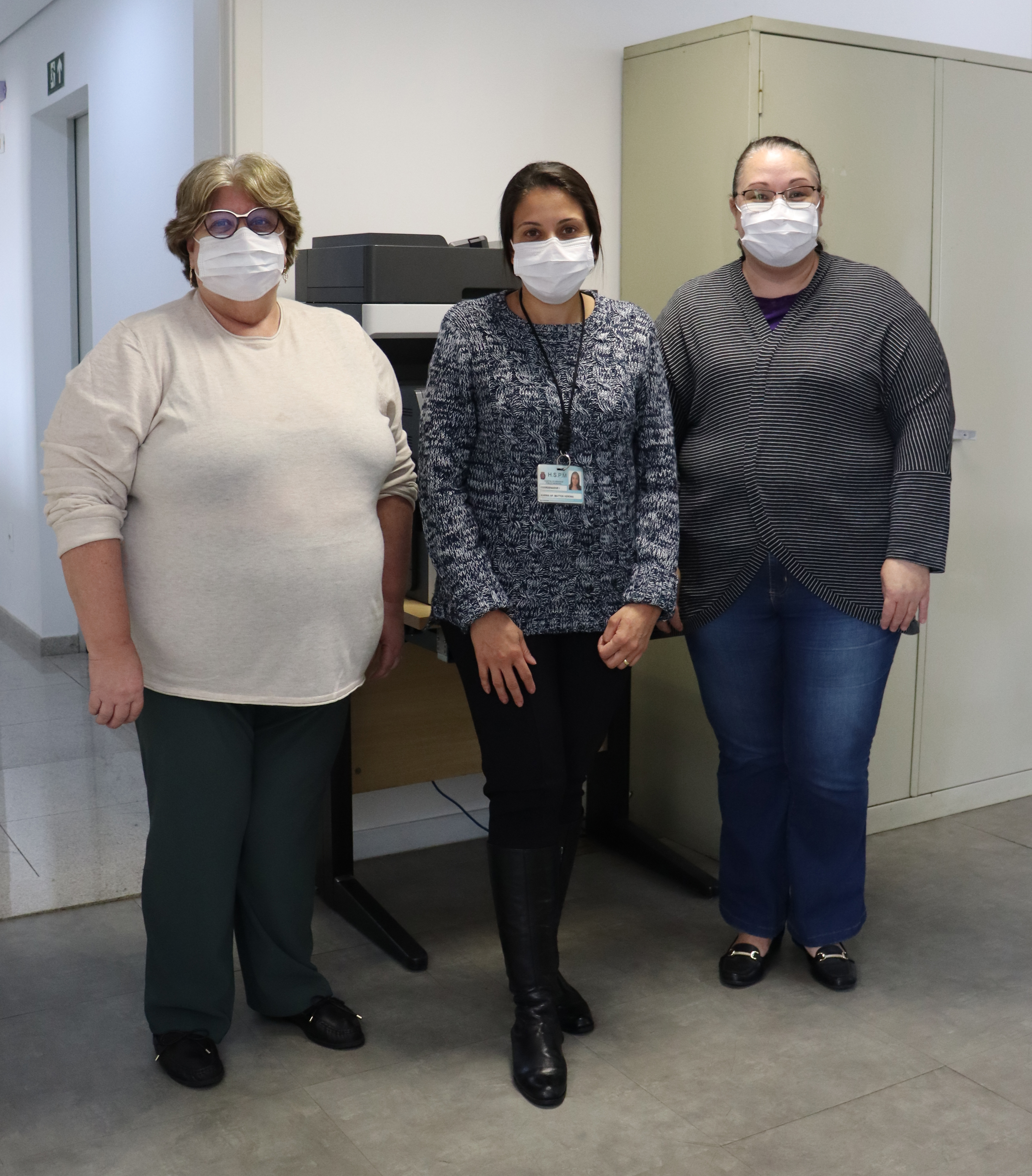 Foto com 3 mulheres da equipe, todas de máscara, as duas dos cantos usam óculos de grau.