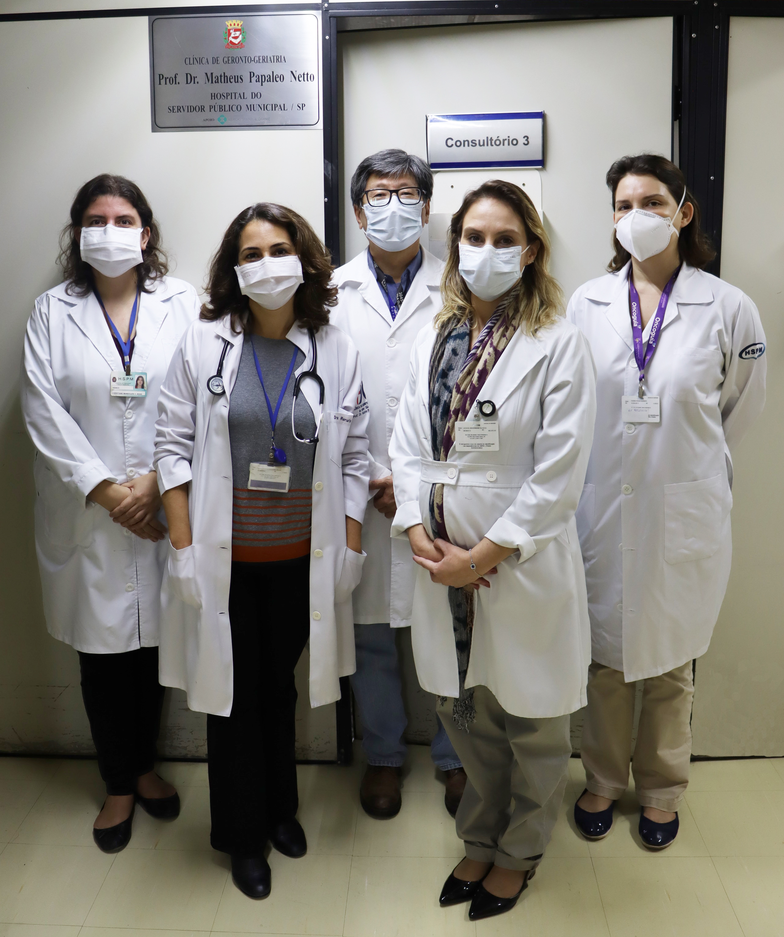 Foto com cinco médicos geriatras do hospital, em frente a um dos consultórios