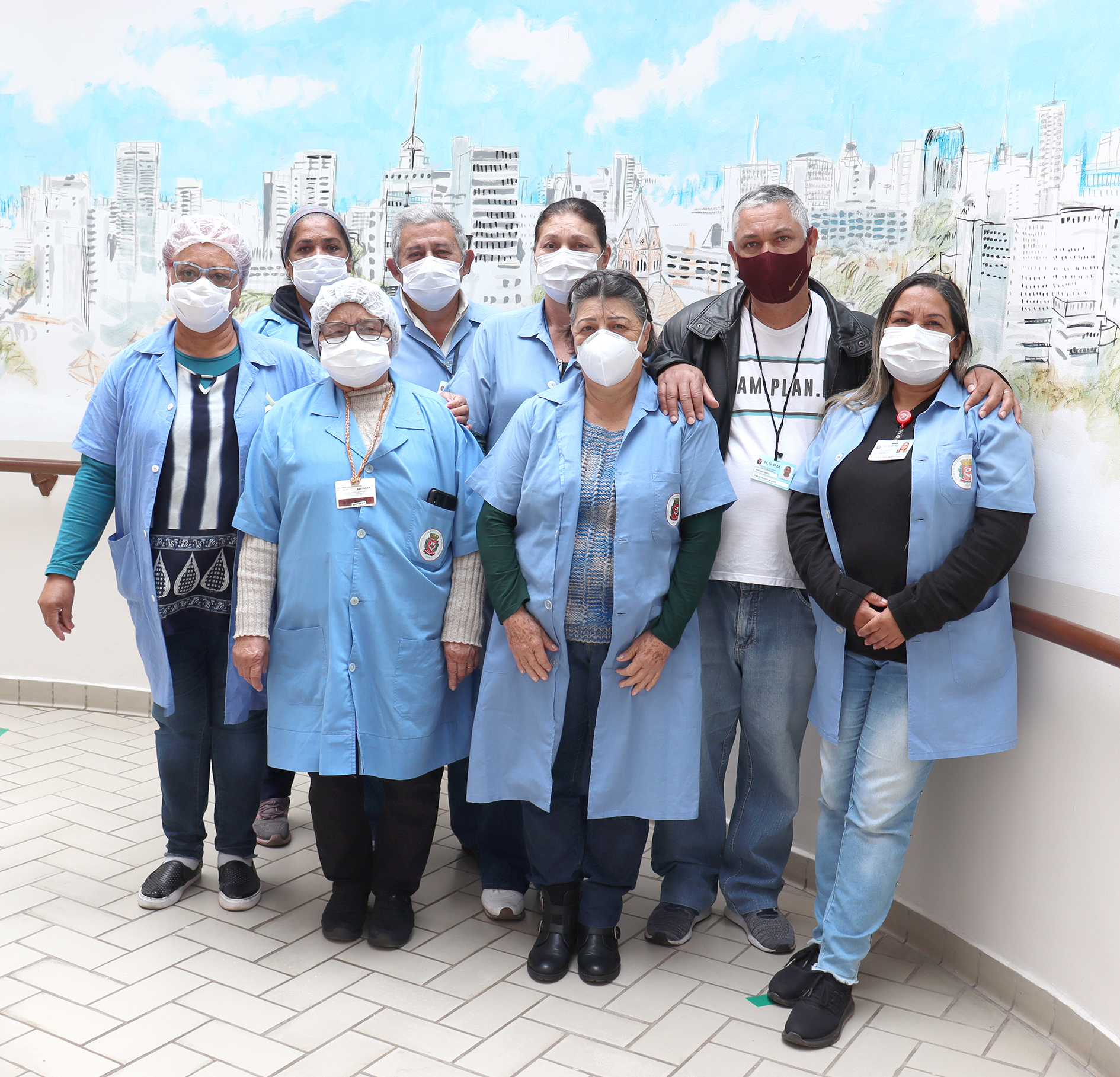 foto de parte da equipe, todos de avental azul, em frente a uma parede decorada