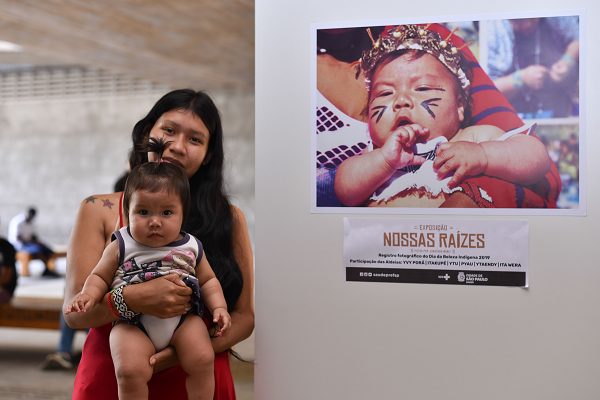 #PraCegoVer: Na imagem, fotografia de uma indígena, segurando uma criança no colo. Ao lado da mulher, fotografia de uma outra criança recém nascida.