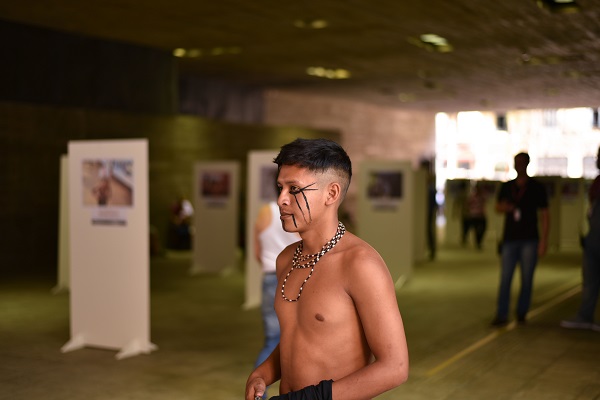 #PraCegoVer: Na imagem, fotografia de um indígena, ele está em pé, praticando suas culturas.