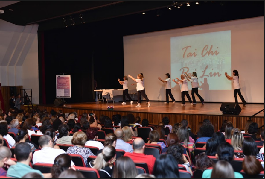 Grupo apresenta Tai Chi Pai Lin no palco. Há dezenas de pessoas na plateia