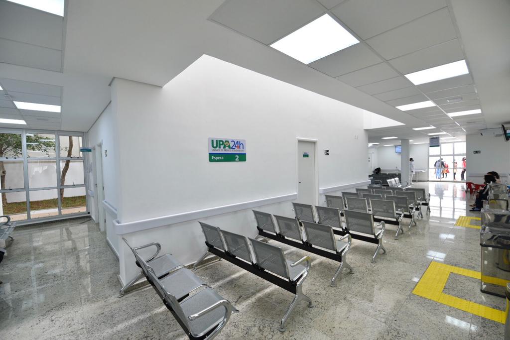 Foto de uma sala de espera. Em uma parede branca há uma placa com a inscrição 