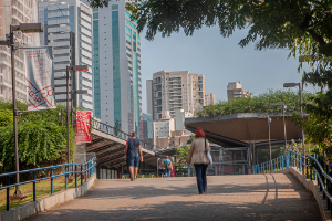 Pessoas andando sobre uma rampa larga de acesso ao Centro Cultural, com vegetacoes nos cantos e predios modernos ao fundo