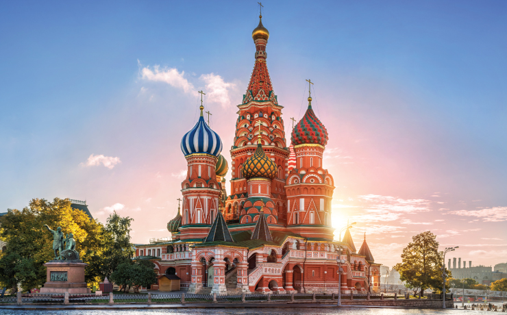 Foto da Catedral de São Basílio em Moscow. Ela é tem cores vermelha, verde, amarela e rosa. Ao fundo o nascer do sol.