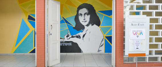 Entrada da biblioteca Anne Frank com as portas abertas exibindo o mural com a pintura de Anne Frank