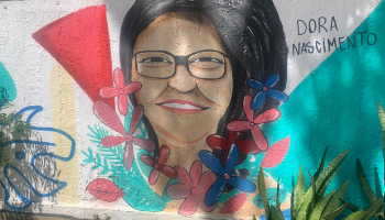 Parede pintada com rosto de uma mulher de oculos  cabelo preto liso, cercada por flores.