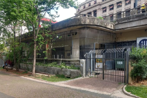 Fachada de edifício térreo em concreto, com gradis em torno dos pilares e arvores em frente