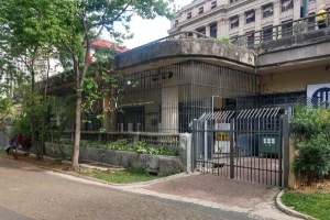 Fachada de edificio terreo em concreto, com gradis em torno dos pilares e arvores em frente