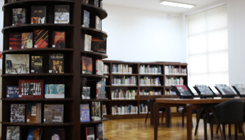 Imagem de livros dispostos na prateleira e na sua frente uma mesa com outros livros expostos.
