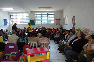 Diversas pessoas assistindo um músico ao violão e uma cantora, sentados dentro da biblioteca