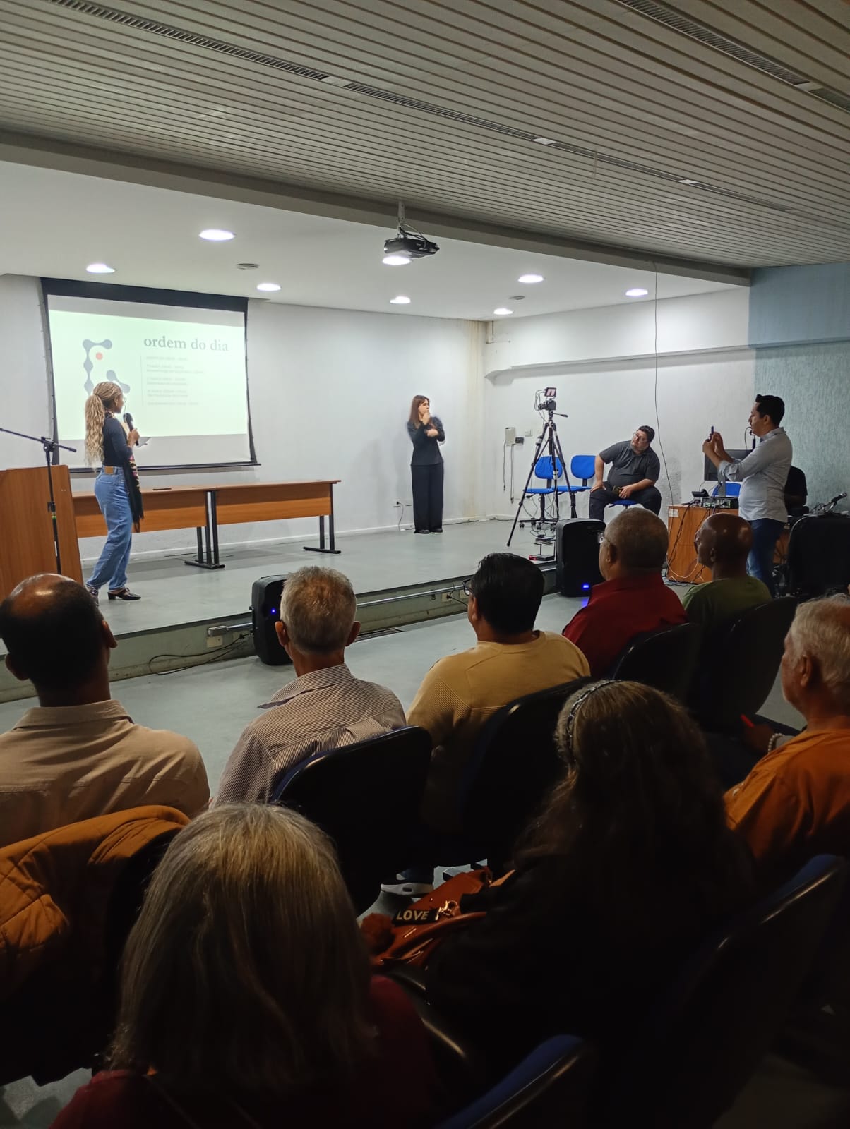 A imagem mostra funcionários públicos apresentando projetos de Orçamento Público com munícipes assistindo