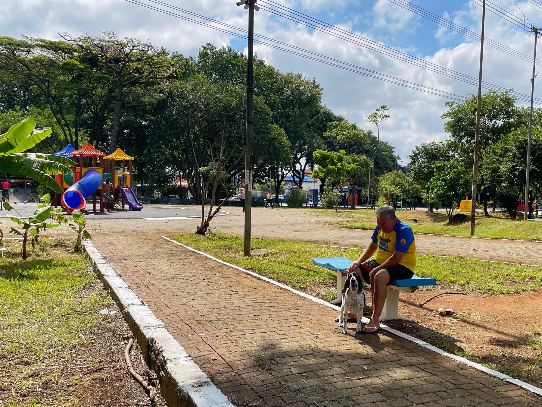 #PraTodosVerem: Imagem mostra a área verde da Praça do Vinho com playground ao fundo e um morador com seu cachorro à direita